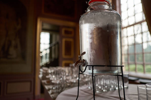 Glass beverage dispenser with fresh water, placed on a table with empty glasses, in a luxurious event setting