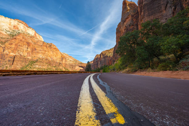 A breathtaking view of a scenic highway cutting through the towering sandstone formations of Zion National Park, Utah. The rugged red rock landscape, dramatic cliffs, and open road create the perfect setting for an unforgettable desert road trip and adventure photography.