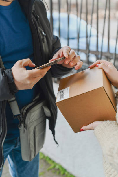 istock Delivery Guy Scanning Package Barcode with Phone Before Handing Over to Female Customer 2202309948