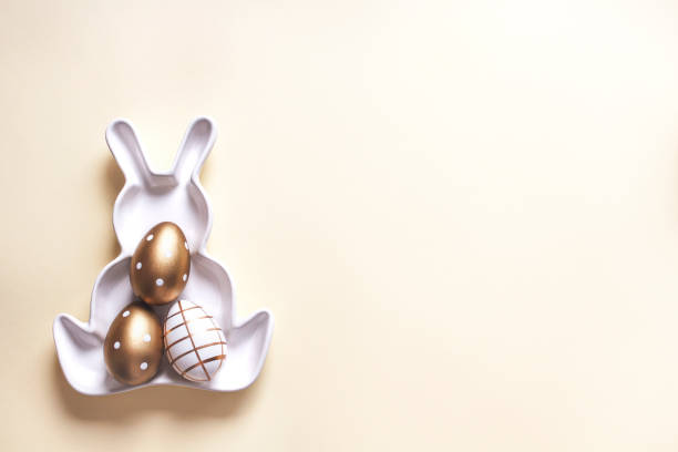 Happy Easter horizontal banner template. Modern dyed and golden Easter eggs on plate in form of Easter bunny on pastel yellow background. Top view, flat lay, copy space.