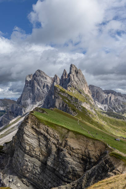 Vertical image of Seceda in the Dolomites, Italy, highlighting dramatic rock formations, grassy slopes, and a dynamic sky, popular for outdoor adventures and trekking