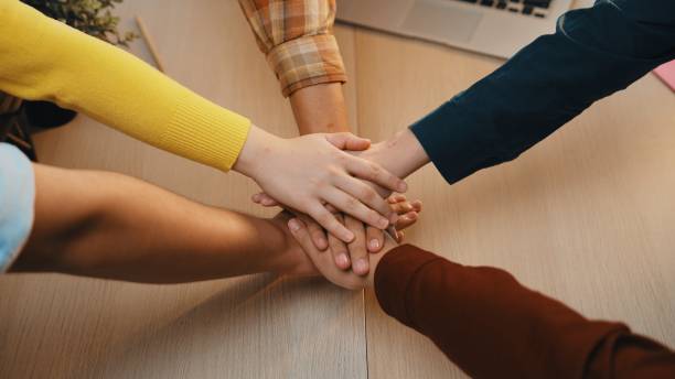 istock Diverse group of individuals joining hands in a supportive manner on a wooden table during a collaborative meeting in a bright workspace SACTR 2202320170