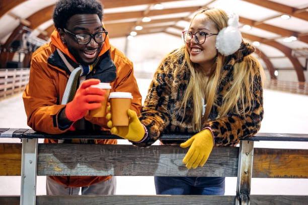 Friends enjoying ice skating together and taking a break for a cup of hot coffee in disposable cup