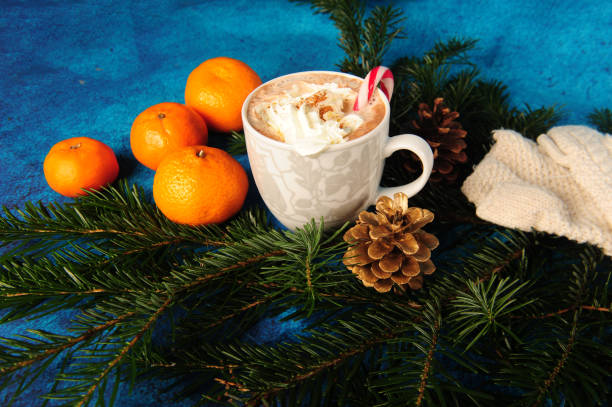 Cup with cocoa and cream with candy kane. Four tangerines. Spruce twig decor with golden and natural pinecones.