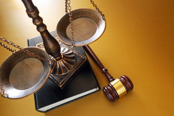 A justice scale rests on top of a law book next to a gavel on a golden background.