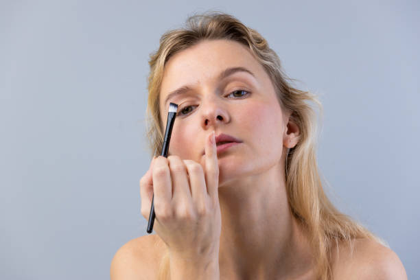 istock Elegant Beauty Routine: A Young Woman Applying Eye Makeup with Precision While Maintaining a Natural Look Against a Soft Gray Background 2202329105