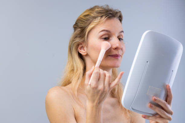 istock A Young Woman Applying Makeup with a Soft Brush While Looking in a Mirror: Embracing Beauty and Self-Care in a Calm and Simple Environment 2202329474