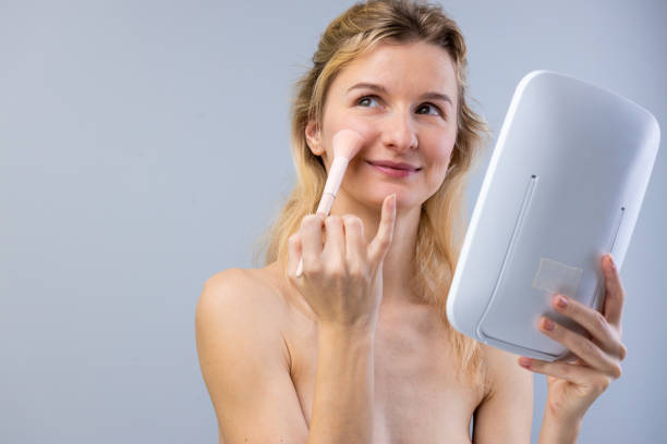 istock A Young Woman Applying Makeup with a Blush Brush in Front of a Mirror, Emphasizing Natural Beauty and Self-Care in a Minimalistic Environment 2202329533