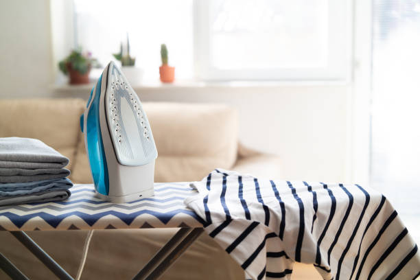 istock Electric iron and pile of clothes on ironing board 2202331471