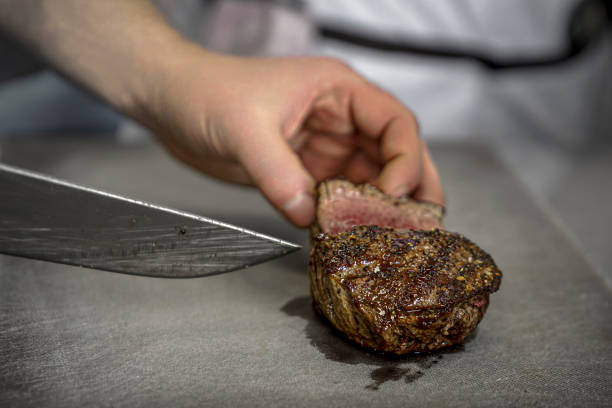 istock restaurant kitchen, a cook cuts a meat steak with a knife, medium frying, blood is coming from the steak, the work of the cooks 2202331559