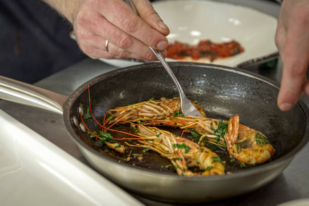 restaurant kitchen, the chef is preparing large shrimp, grilling on a frying pan, splashes of oil are flying and steam is coming, the work of the cooks.