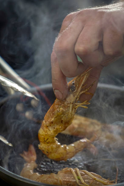 istock restaurant kitchen, the chef is preparing large shrimp, grilling on a frying pan, splashes of oil are flying and steam is coming, the work of the cooks 2202331632