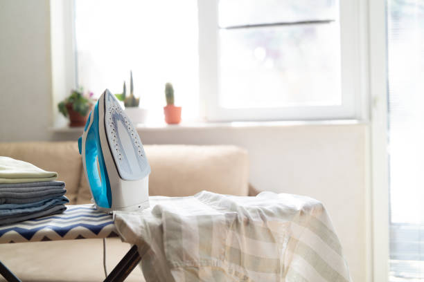 istock Electric iron and pile of clothes on ironing board 2202331847