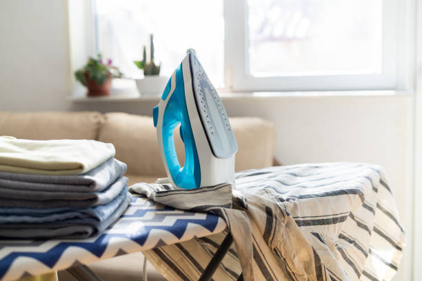 istock Electric iron and pile of clothes on ironing board 2202331973