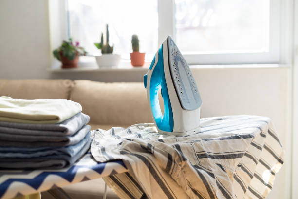 istock Electric iron and pile of clothes on ironing board 2202331999