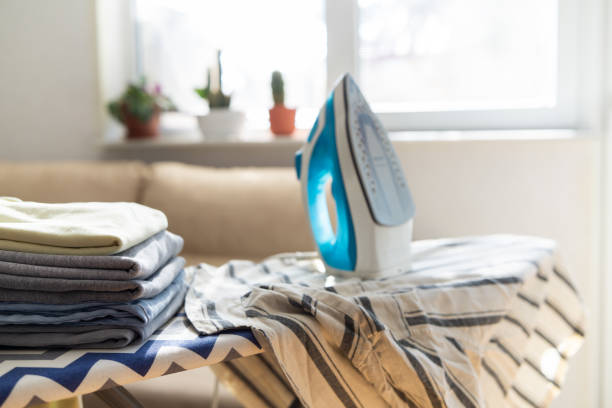 istock Electric iron and pile of clothes on ironing board 2202332002