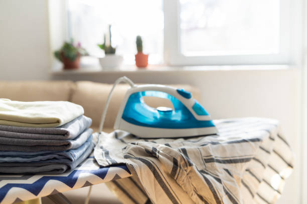 istock Electric iron and pile of clothes on ironing board 2202332067