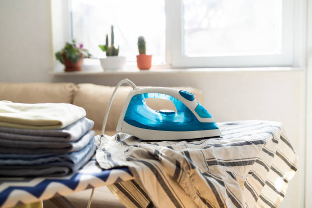 istock Electric iron and pile of clothes on ironing board 2202332073