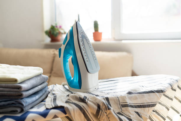 istock Electric iron and pile of clothes on ironing board 2202332172