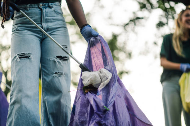 istock Volunteer picking up trash in park holding purple garbage bag 2202333597