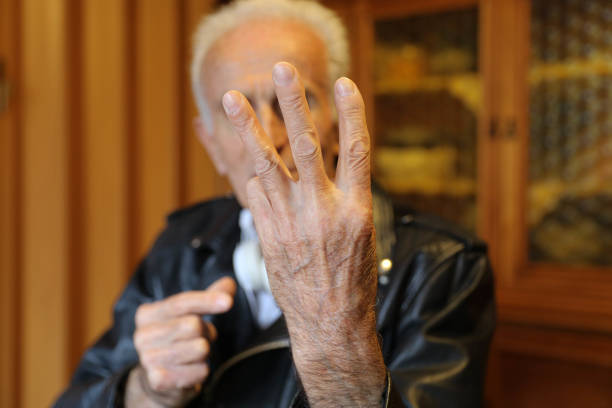 An elderly man showing an open hand, using his fingers to indicate numbers.