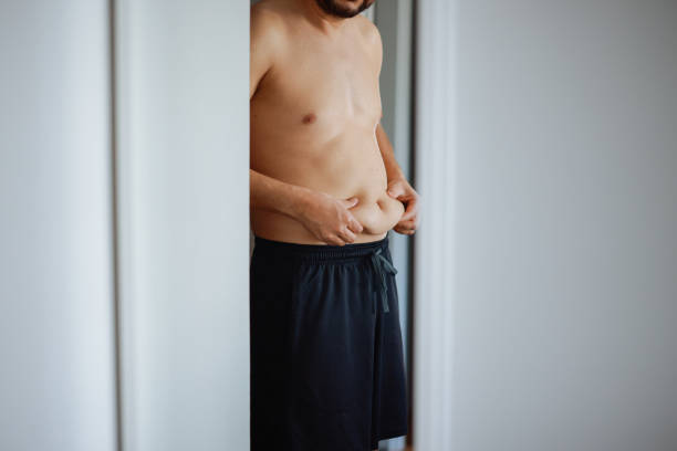 istock Overweight man checking his fat body reflection in mirror 2202335640