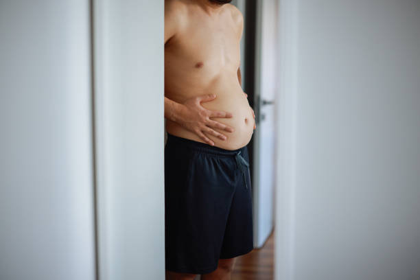 istock Overweight man checking his fat body reflection in mirror 2202338775