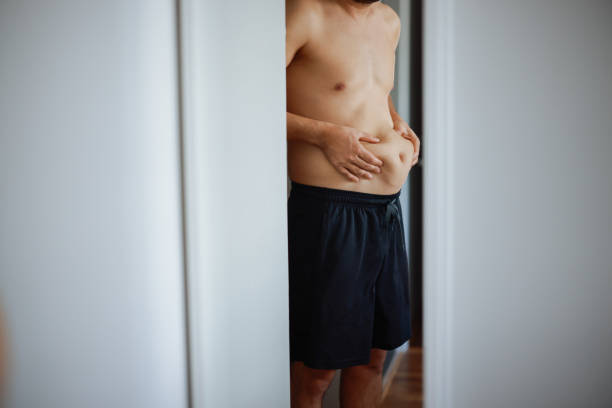 istock Overweight man checking his fat body reflection in mirror 2202338886