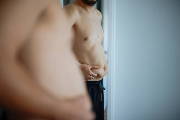 Overweight man checking his fat body reflection in mirror