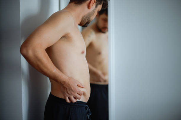 istock Overweight man checking his fat body reflection in mirror 2202339237
