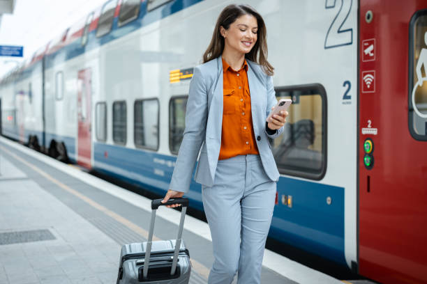 istock Elegant business woman is pulling a suitcase and using the phone at the train station 2202343096