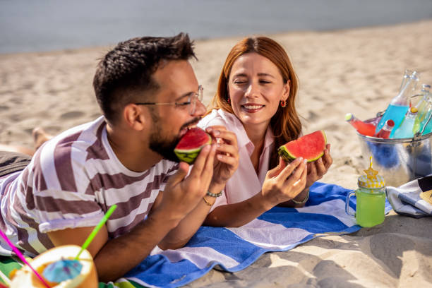 istock Two friends on a beach eating watermelon. 2202346289