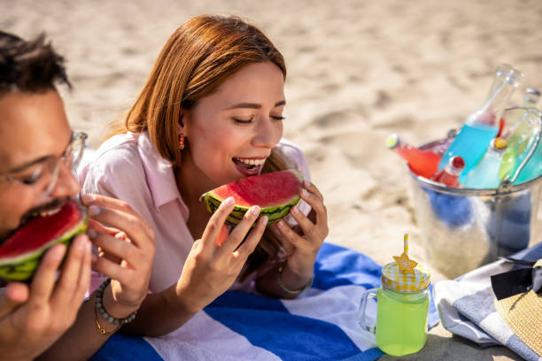 istock Two friends on a beach eating watermelon. 2202346348