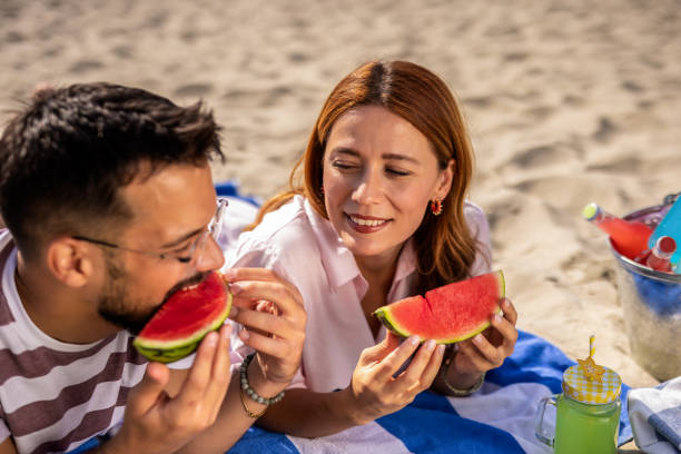 istock Two friends on a beach eating watermelon. 2202346349