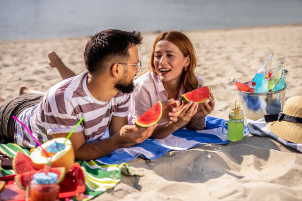 istock Two friends on a beach eating watermelon. 2202346350