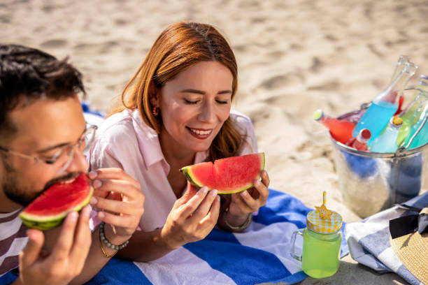 istock Two friends on a beach eating watermelon. 2202346352