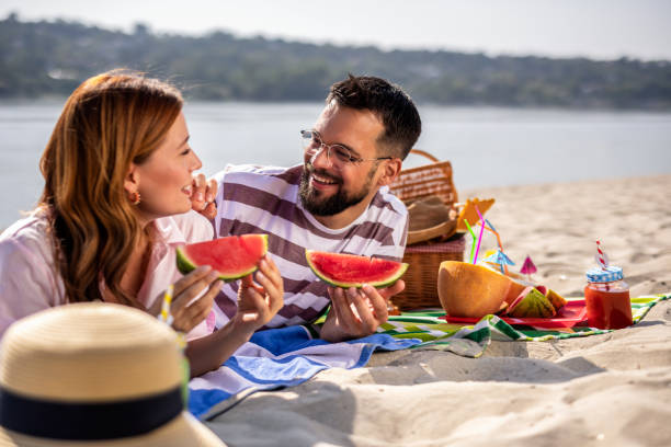 istock Two friends on a beach eating watermelon. 2202346399