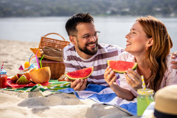istock Two friends on a beach eating watermelon. 2202346403