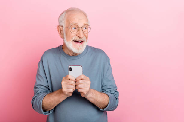istock Photo of funny excited retired man grey sweater spectacles looking empty space chatting gadget isolated pink color background 2202361002