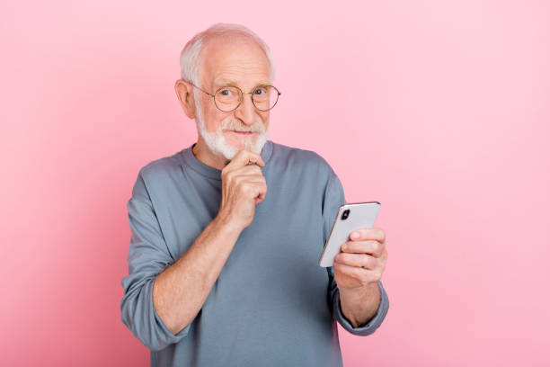 istock Photo of positive tricky guy pensioner dressed grey pullover glasses reading modern device isolated pink color background 2202361017