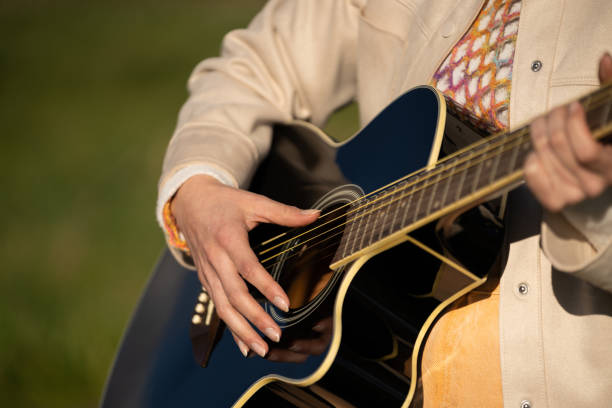 istock Woman playing acoustic guitar outdoors, fingers gracefully strumming strings, creating peaceful melodic moment against natural backdrop 2202361354