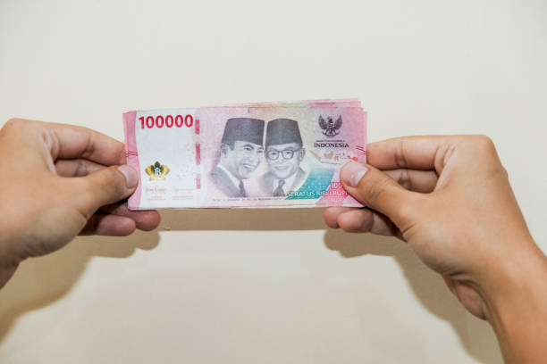 istock A man hand Holding hundred thousand rupiah cream background 2202362443