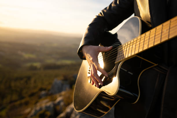 Musician's hand strumming acoustic guitar strings, golden sunset illuminating rustic landscape with warm, emotive musical ambiance