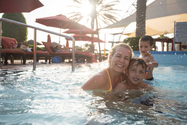 Happy little boy enjoying in his mother hug with great affection during summer day at pool.