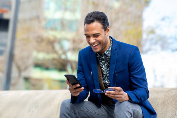 istock Black businessman sitting outside using phone and laughing 2202381302
