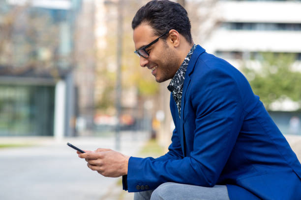 istock Happy black businessman sitting outside using cell phone 2202381304