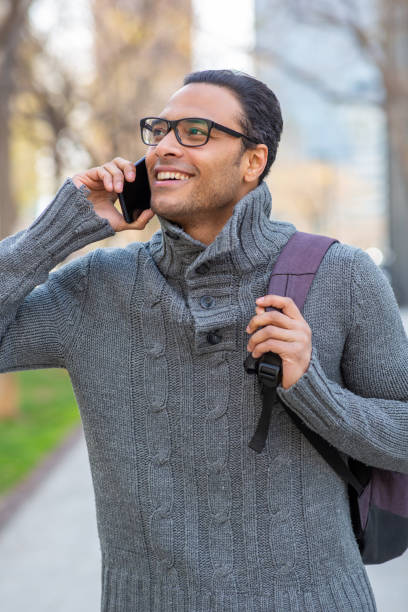 istock Smiling young african man talking on cell phone with bag outside 2202381424