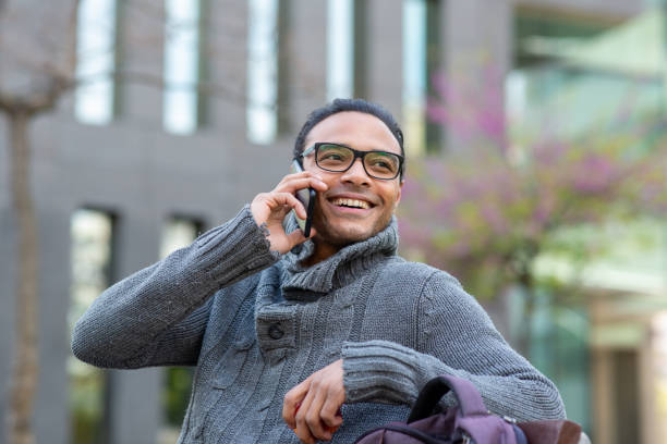 istock Young african man talking on cell phone while sitting on bench outside in city 2202381444