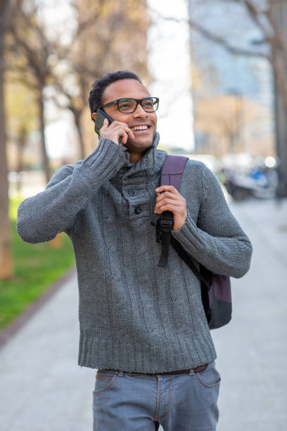 istock Good looking young african guy with bag walking outside and talking on cell phone 2202381498