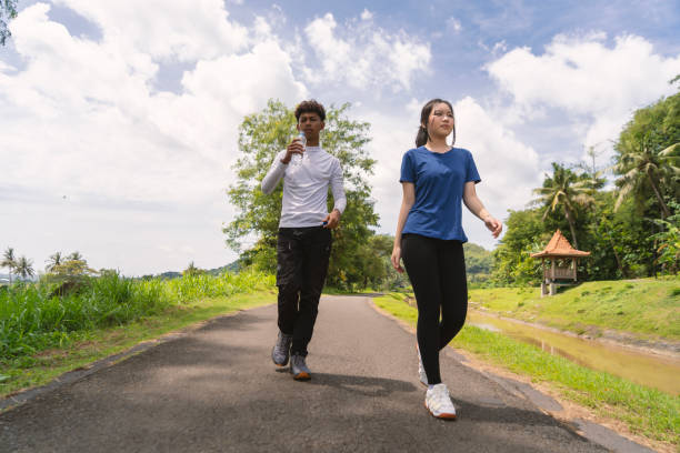 istock active young asian couple holding water bottle while walking exercise at rural area 2202397728